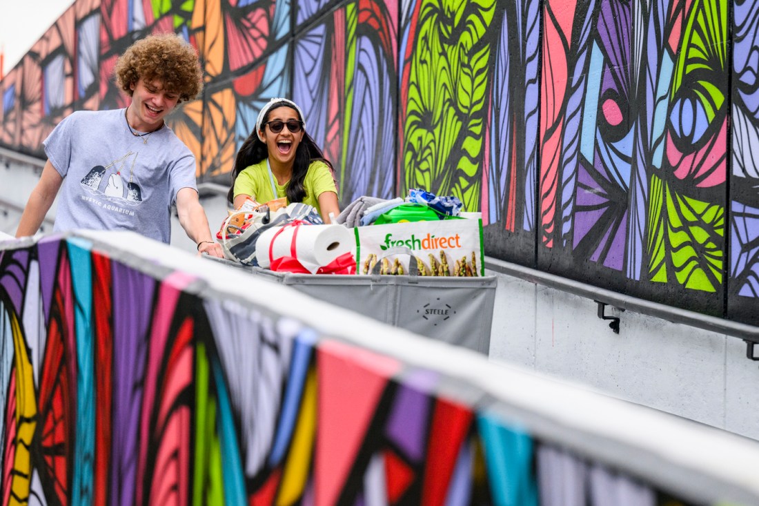 Students push a bin of belongings along a colorful mural during move-in day.