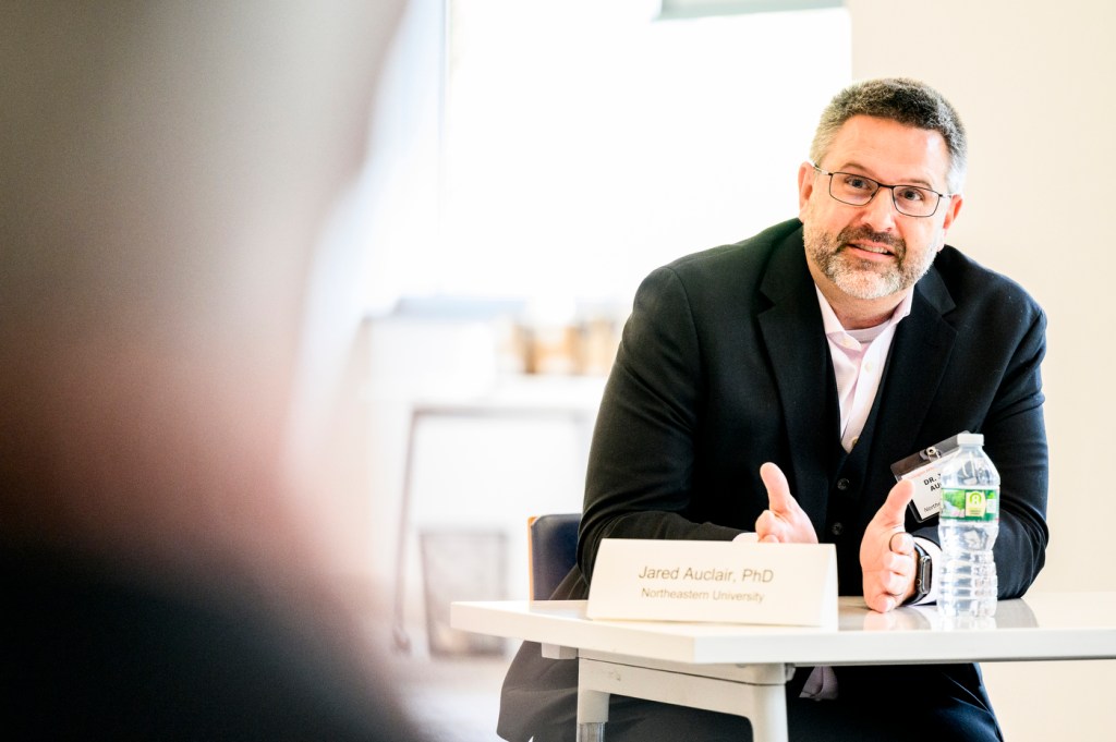 A person speaks at a table during a discussion event indoors.