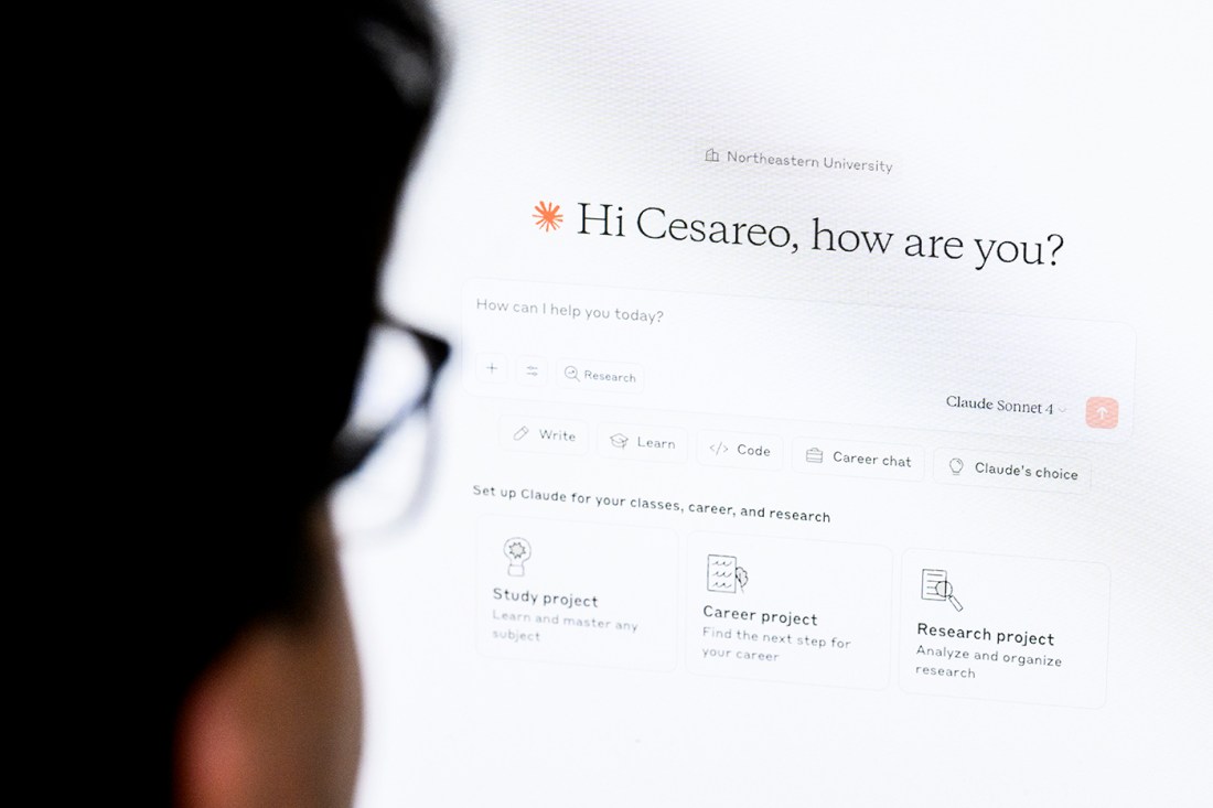 The silhouette of a person's head seen from behind as they look at a screen open to Claude AI, which says 'Hi Cesareo, how are you?' atop a prompt box.