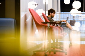 A person works on a laptop while seated in a brightly lit indoor space.