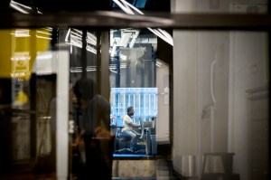 A person is seen working in a well-lit space, framed by reflections and structural elements.