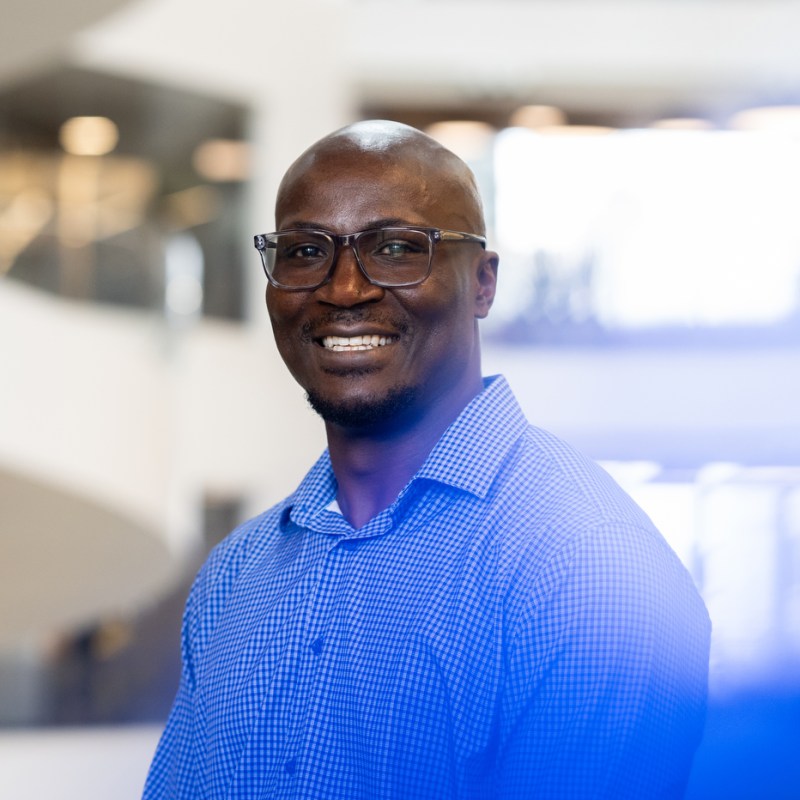 Portrait of Francis Oywech wearing glasses and a blue button down with a checked pattern on it.