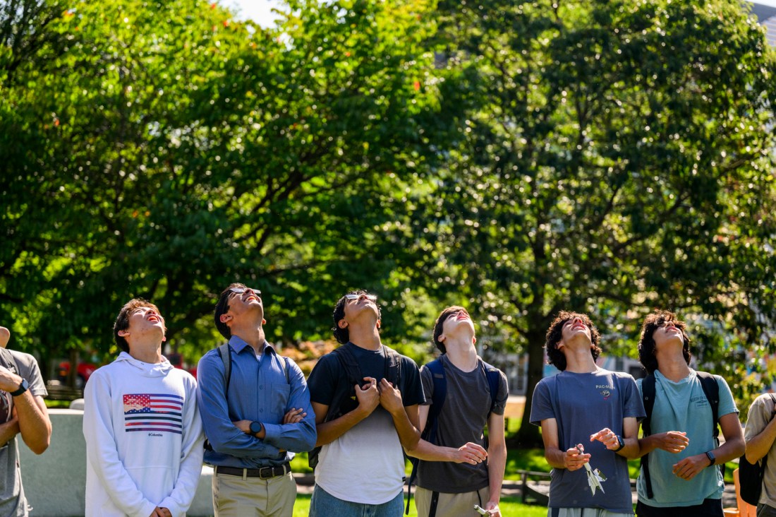 A group of students outside looking up watching model rockets.