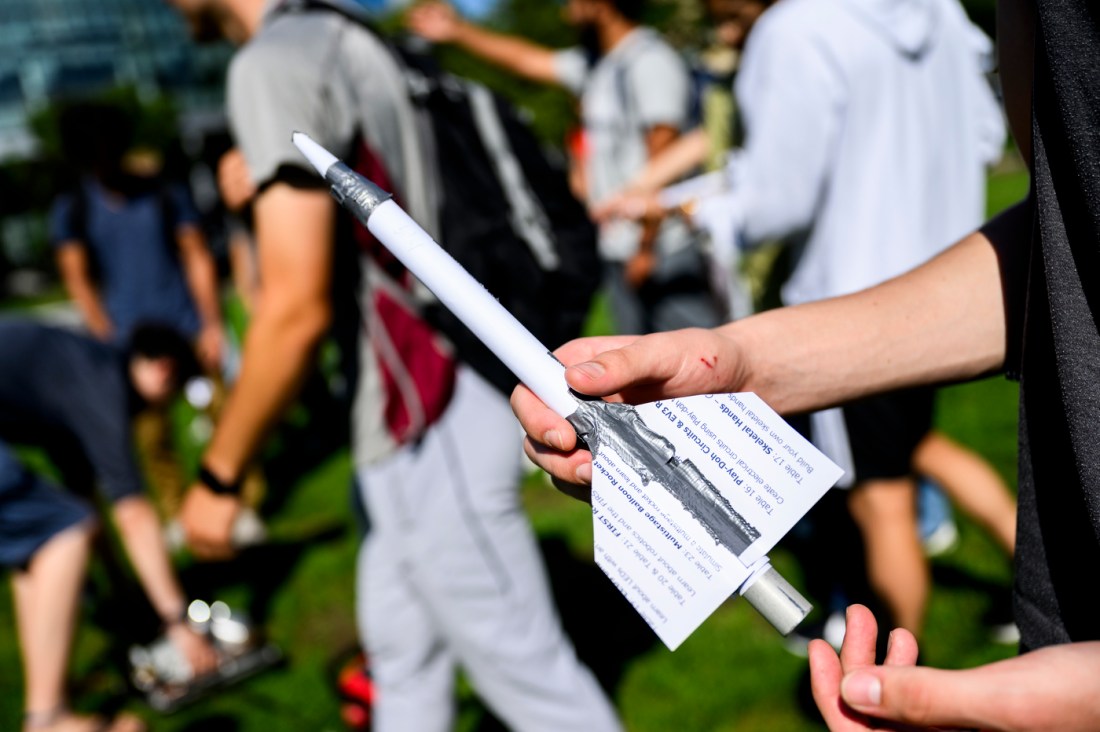 Students outside walking in the background, where in the foreground someone shows their model rocket.