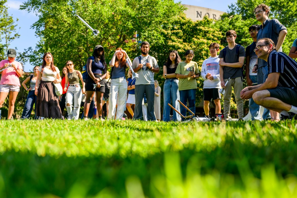 A group of people watches an outdoor activity on a sunny day.
