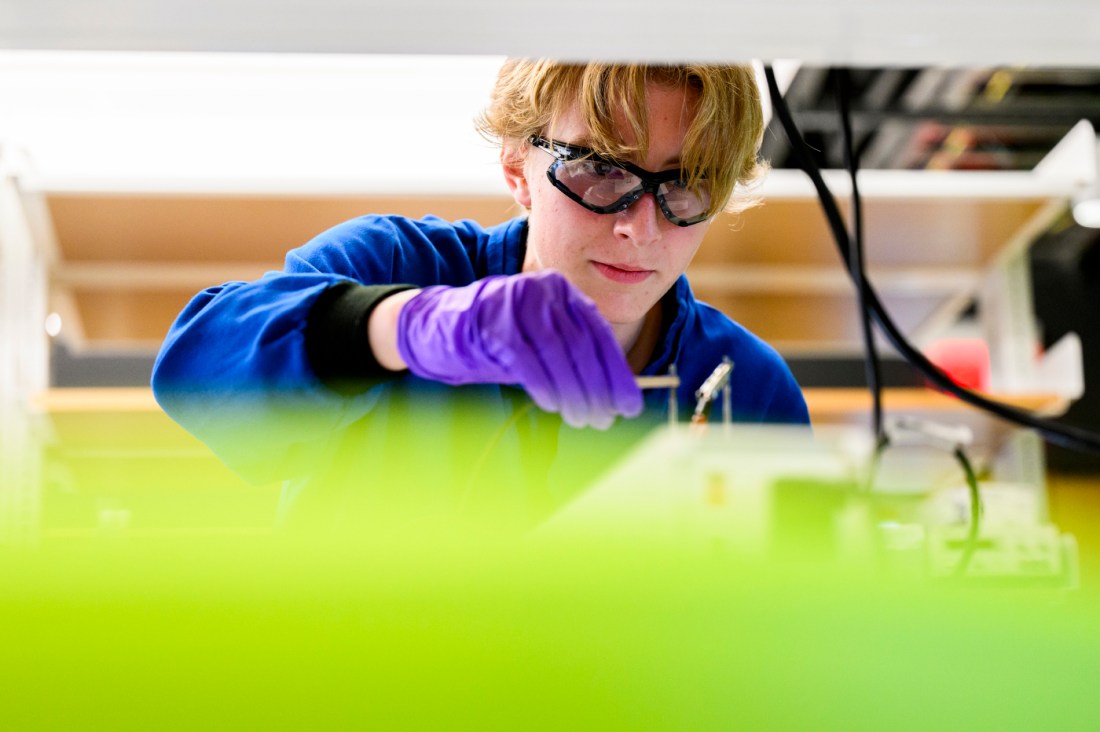A student wearing gloves and goggles working in a lab setting.