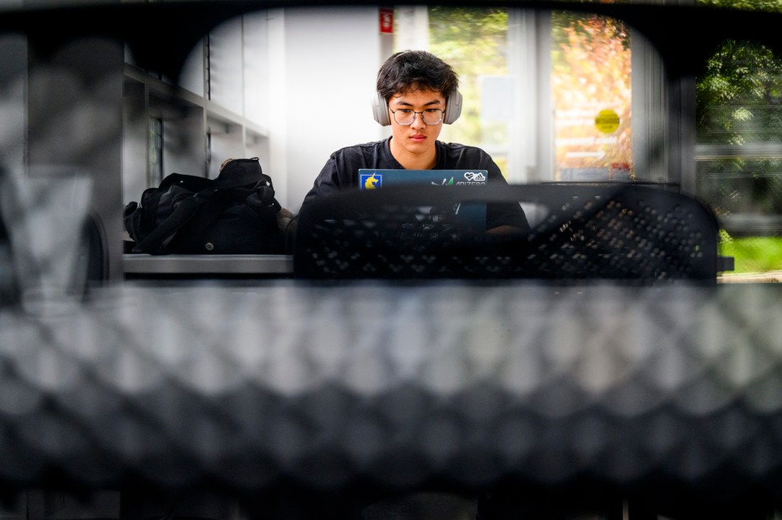A Northeastern student in a black shirt seen working on a computer with headphones on.