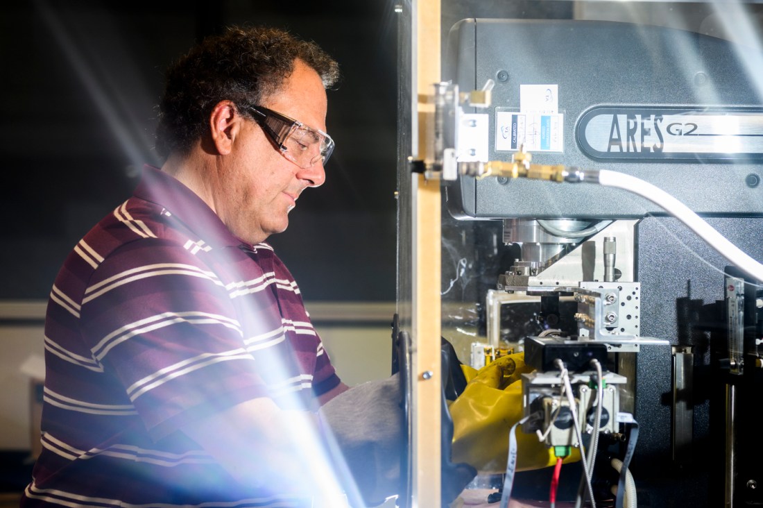 Steve Lustig wearing safety glasses and a maroon striped polo shirt operating laboratory equipment at Northeastern University.