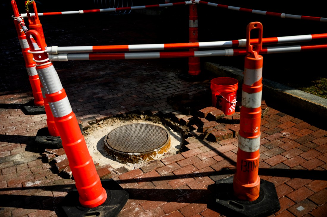 A series of white and orange construction cones around a manhole in the brick.