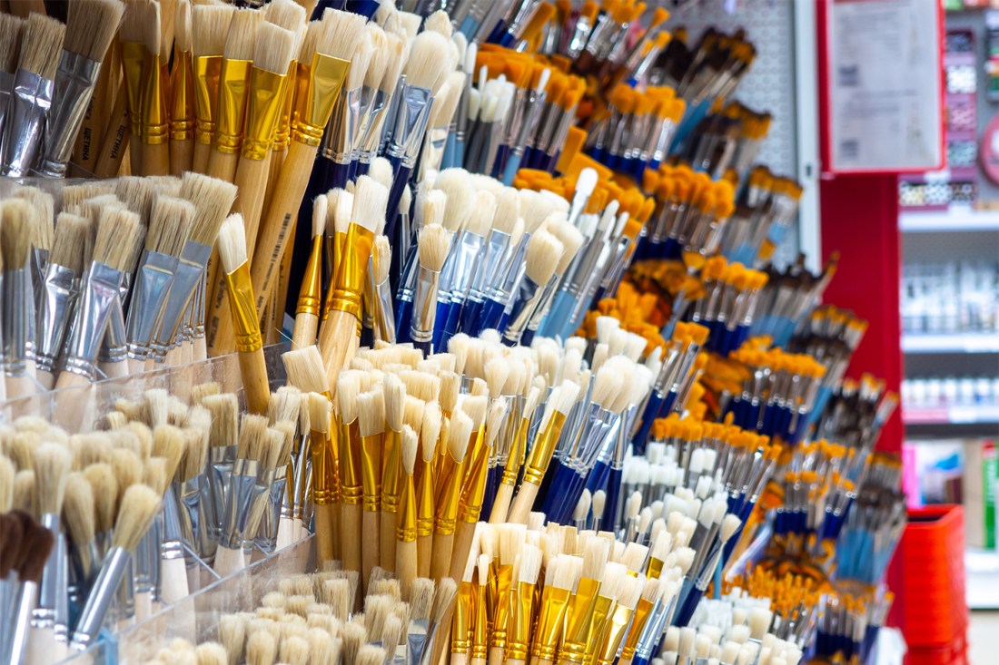Groups of paintbrushes in a row on a wall for sale.