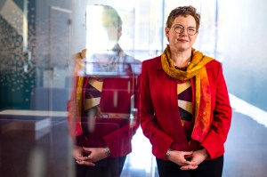 Portrait of Elizabeth Mynatt wearing a red blazer and yellow scarf, leaning up against a glass wall.