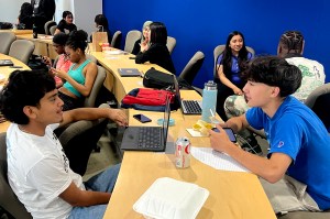 Students sitting on either side of a long table engaged with each other in a summer AI program.