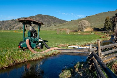 A farmer or rancher in a tractor with a tube going into a river as they manage water flow to their pastures.