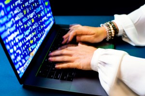 The hands of a person wearing a long-sleeve white blouse and bracelets typing on a laptop.