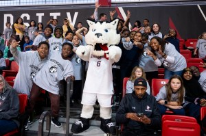 Paws pointing forward, surrounded by kids wearing Northeastern t-shirts in a stadium