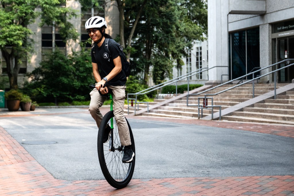A person on a unicycle riding across a campus.