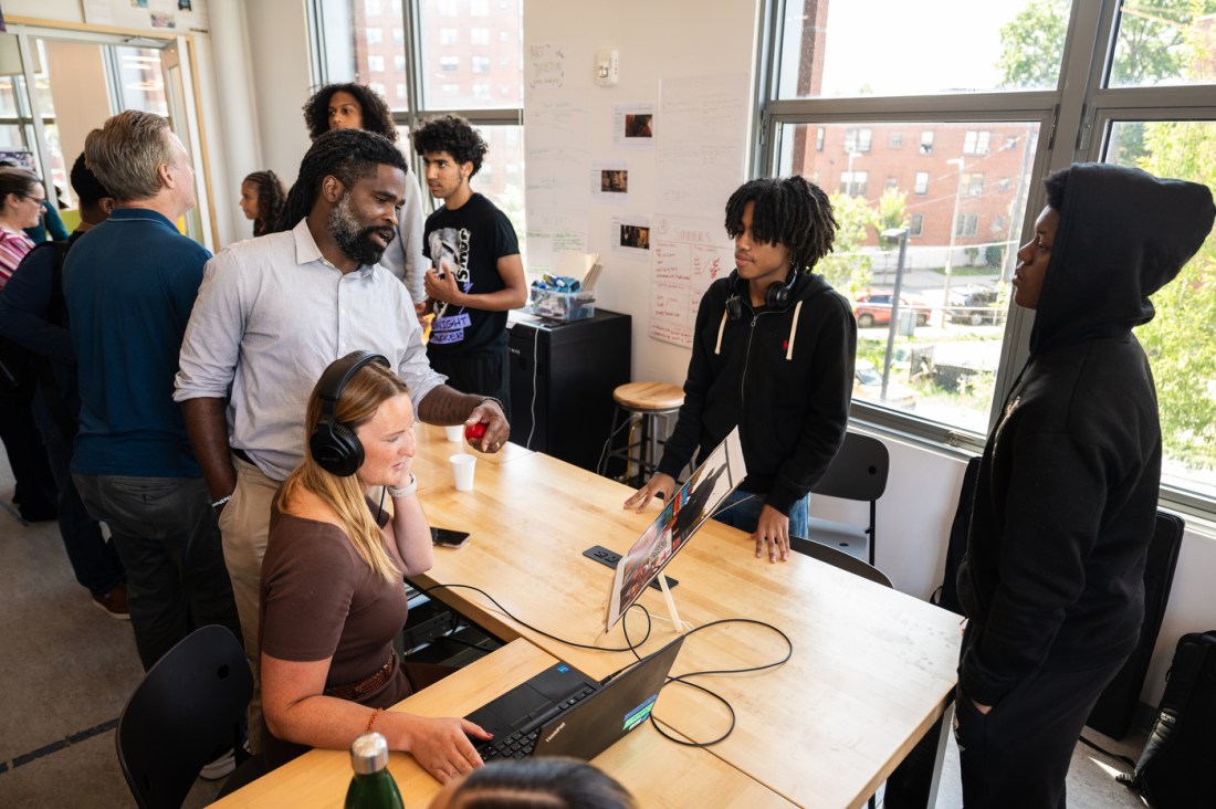 High students cluster around instructors as they evaluate their work on the computer and headphones.