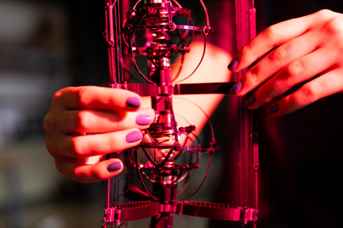 Close-up of two students’ hands with purple nail polish adjusting intricate circular wire components on the SCCRUB robot under red lighting in Northeastern’s EXP robotics bay.