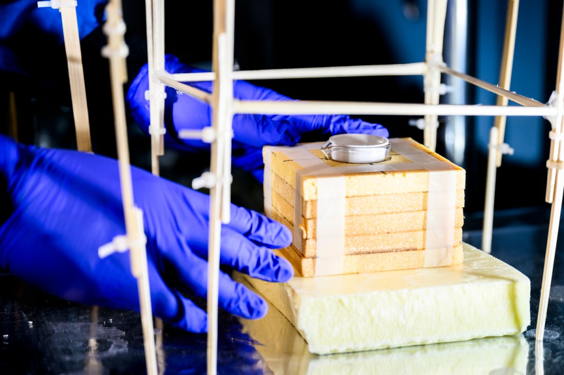 A researcher wearing blue gloves carefully handles a block of insulating foam material within a structural test frame at Northeastern University, part of Yi Zheng’s lab work on solar energy innovations using nanoscale functional materials.