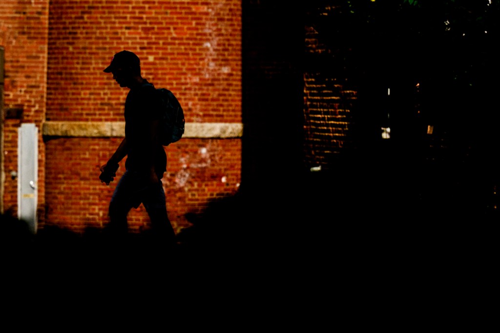 A silhouetted figure of a student walking past a brick building with horizontal windows.
