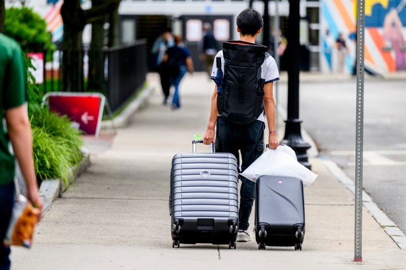A person wheels two suitcases on the sidewalk near Ruggles Station. 