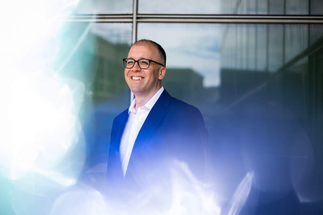 Joshua Merson, a clinical professor at Northeastern University’s Bouve College of Health Sciences, stands outside a campus building, smiling and wearing a blue blazer and glasses.