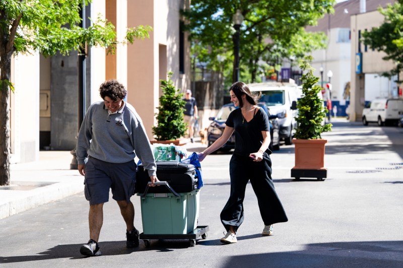 People push a bin and suitcase through the Boston campus.