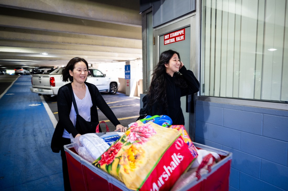 Two Northeastern students roll large suitcases through a parking garage during move-in day, assisted by a family member.