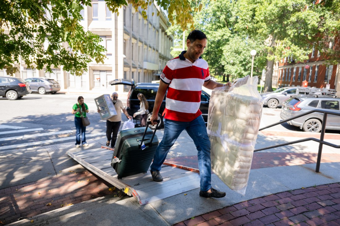A student carries a large plastic-wrapped mattress into the Stetson West dormitory at Northeastern, while parents and movers assist nearby.