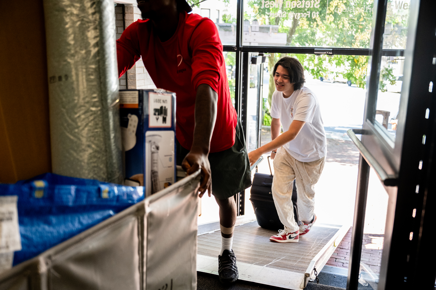 A person pushes a hamper full of move-in supplies while another carries a suitcase.