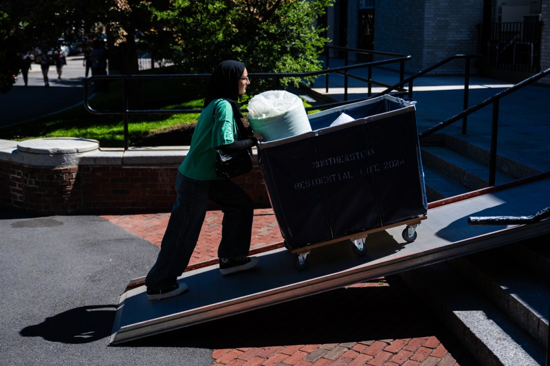 A student pushing a wheeled cart full of their belongings up a ramp.