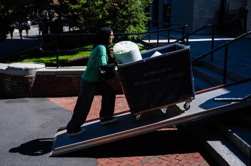 A person pushes a hamper of move-in supplies up a ramp.