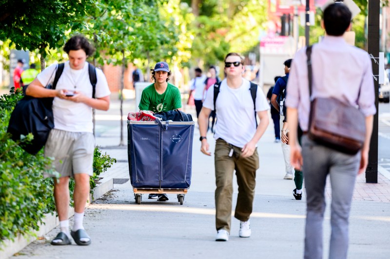 People walk through the Boston campus, including a student pushing a move-in hamper.