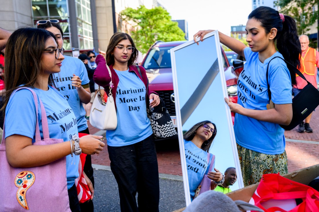Four people wearing matching shirts that say 'Marium's Move In Day' stand around a wheeled cart while one of them places a full length mirror inside.