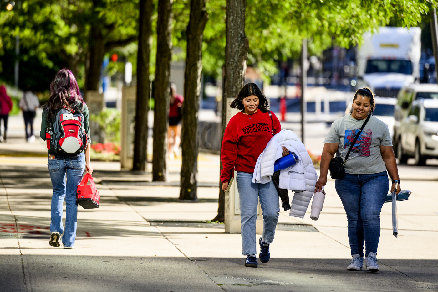 Two people walk down a sidewalk on the Boston campus.