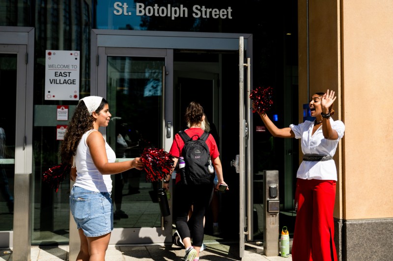A person with pom-poms welcomes students into a dorm.
