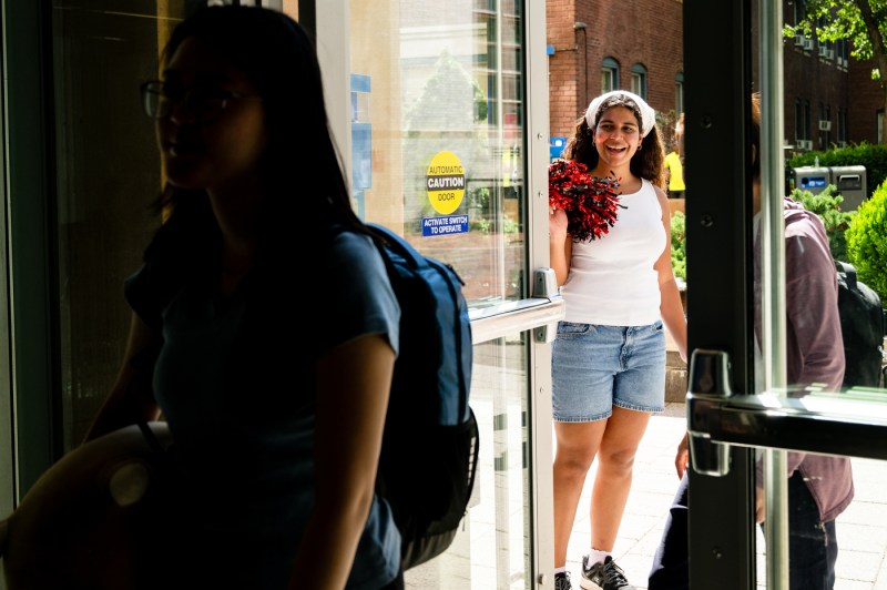 A person with pom-poms welcomes students into a dorm.