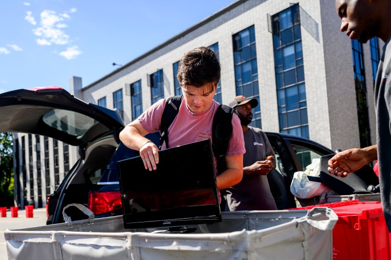 People unload a car and pack a hamper full of move-in supplies.