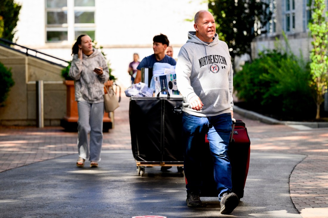 A parent in a grey Northeastern sweatshirt walking on campus during move-in week.