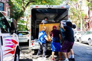Several people work to move a large piece of furniture out of the back of a U-Haul truck.