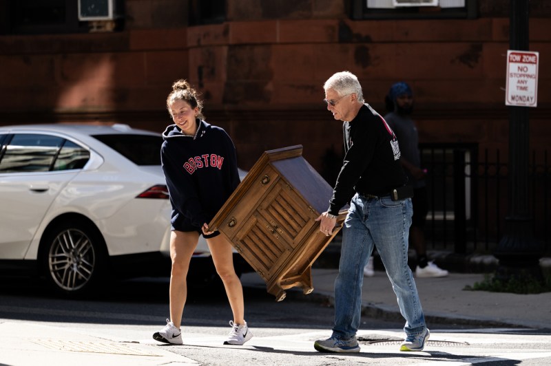 Two people carry a piece of furniture across a street.