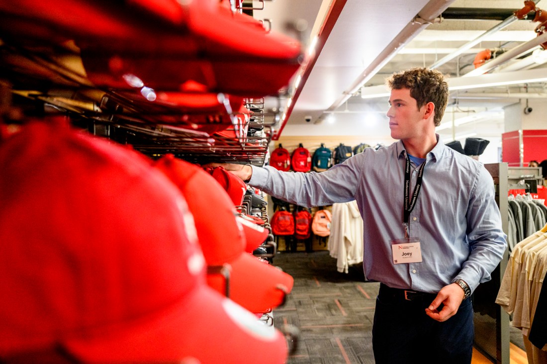 Joe Friedman, the first student CEO of Follett bookstore, reaches for an item on a shelf stocked with red hats.