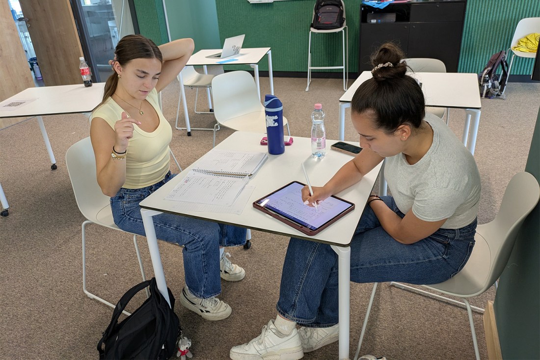 Two students collaborate on math problems using a tablet and notebook in a classroom 