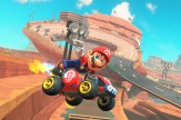 A screen capture of the Mario character in a race car floating in the area over a race track that extends into the background.