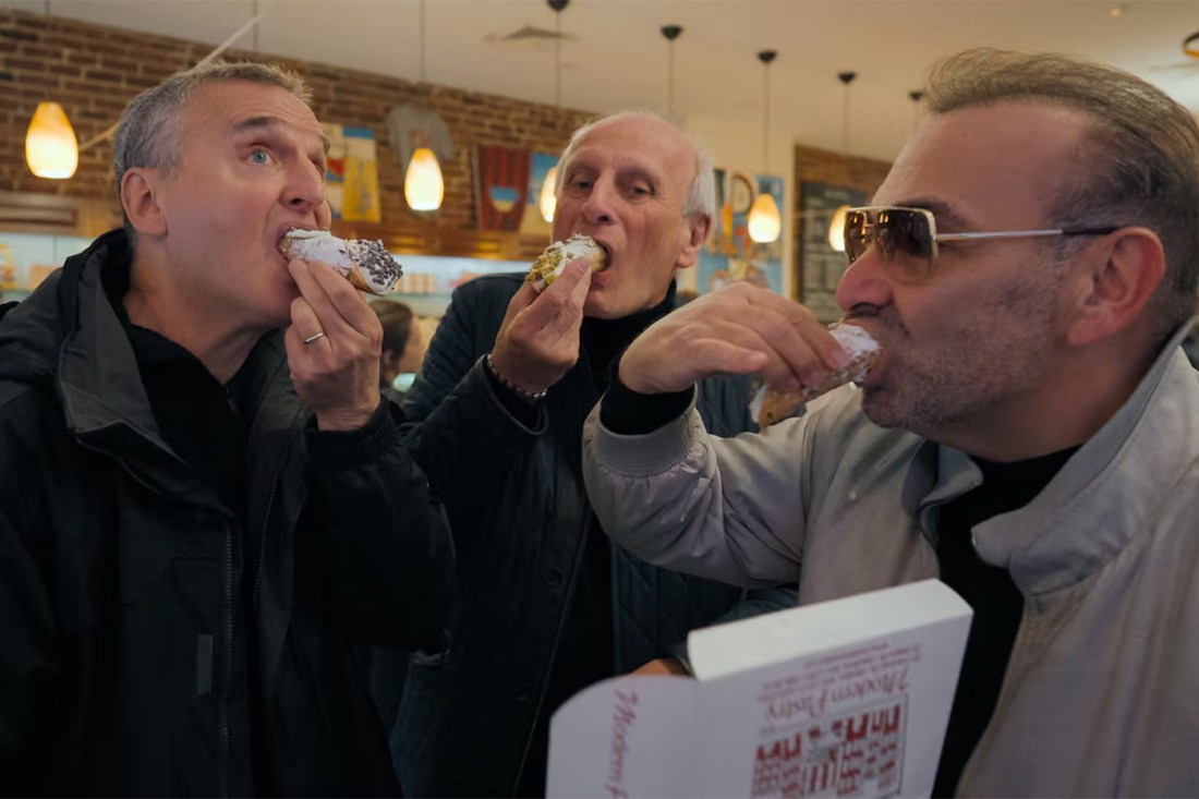 Phil and two other people eat delicious-looking cannolis in a restaurant.