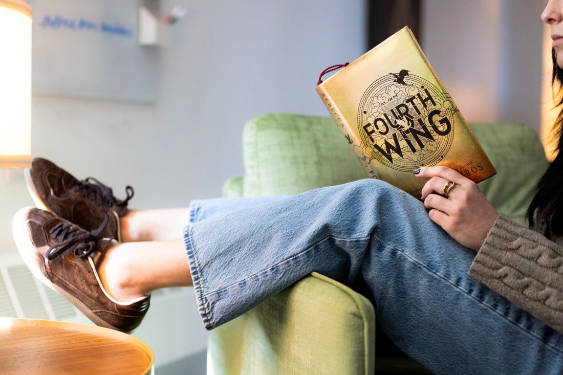 The view of a person's legs and feet as they dangle from a green couch while holding a book.