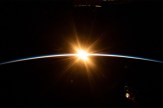A photo of an eclipse. The sun rises over the Earth’s horizon, as seen from space, casting a golden glow against the darkness of space. A thin blue curve marks the planet’s atmosphere.