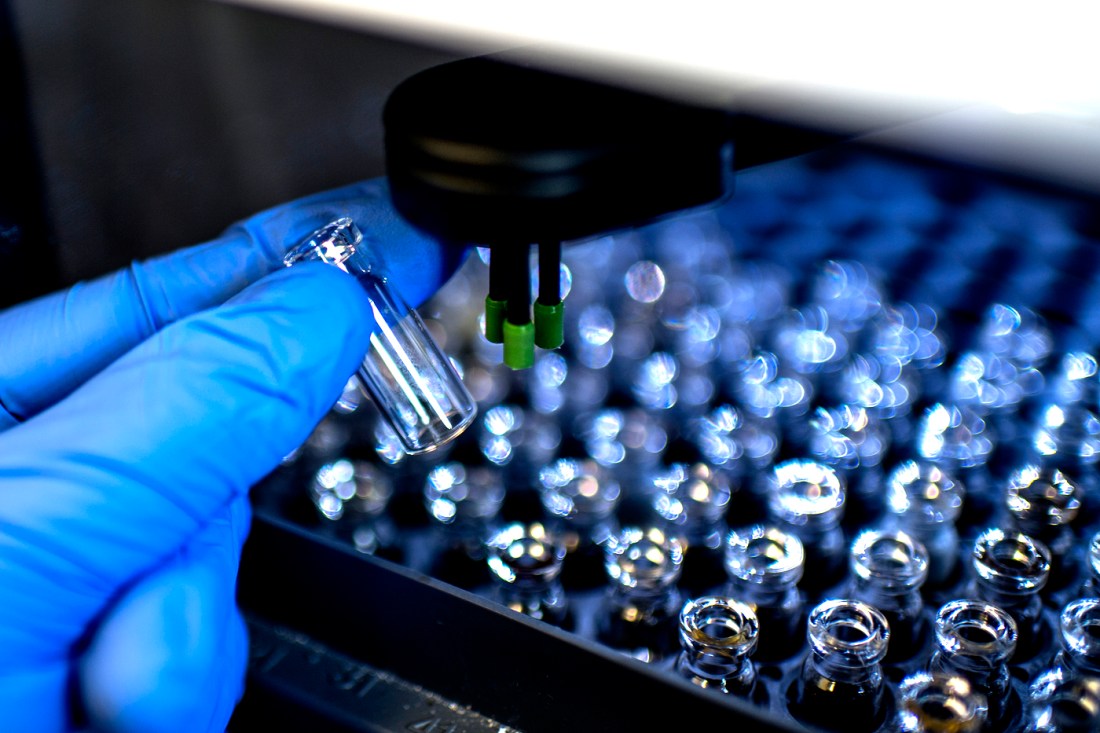 A blue-gloved researcher holds a small vial in a lab.