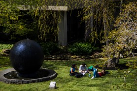 A group of students sit on the grass next to the large, black Koi Pond orb.