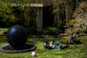 A group of students sit on the grass next to the large, black Koi Pond orb.